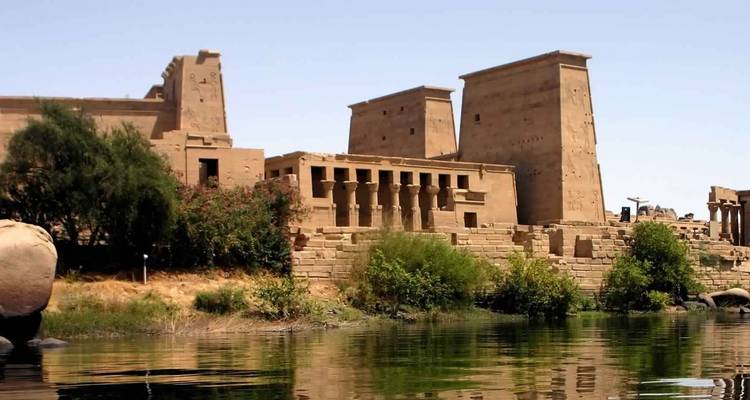 View of an ancient Egyptian temple complex near a river with clear skies.