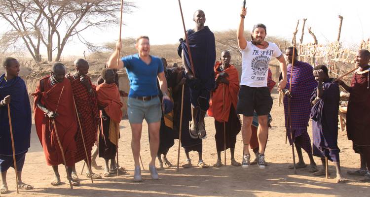Gruppe von Menschen, einige in traditioneller Kleidung, die im Freien springen und lächeln.