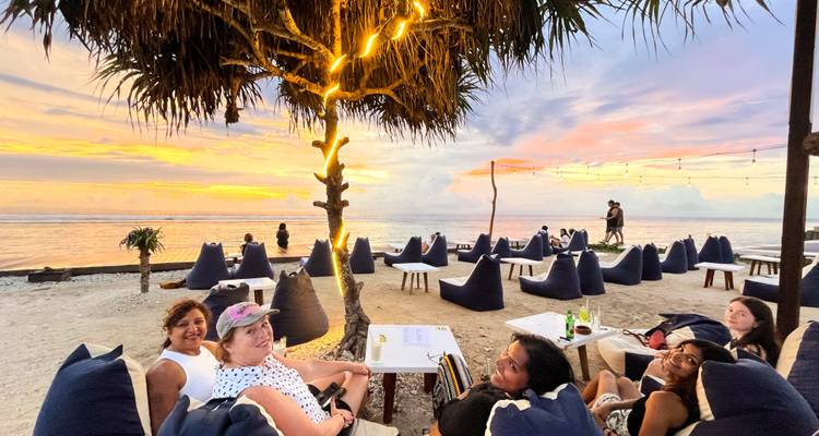 Grupo de personas relajándose en un salón junto a la playa con vistas del atardecer.