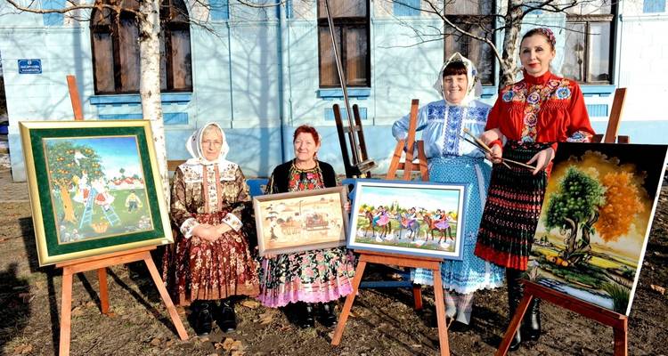 Women in traditional clothing posing with their artwork outdoors.