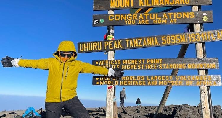 Person celebrating at the Mount Kilimanjaro Uhuru Peak sign.