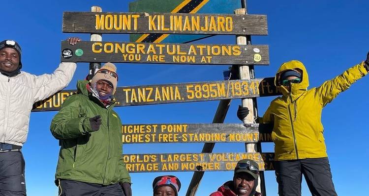 Group of people posing by the Uhuru Peak sign on Mount Kilimanjaro.