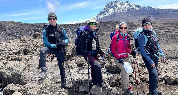 Four hikers posing on a rocky terrain with a mountain in the background.