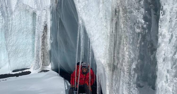 Climber in a red jacket maneuvering through a glacier crevice.