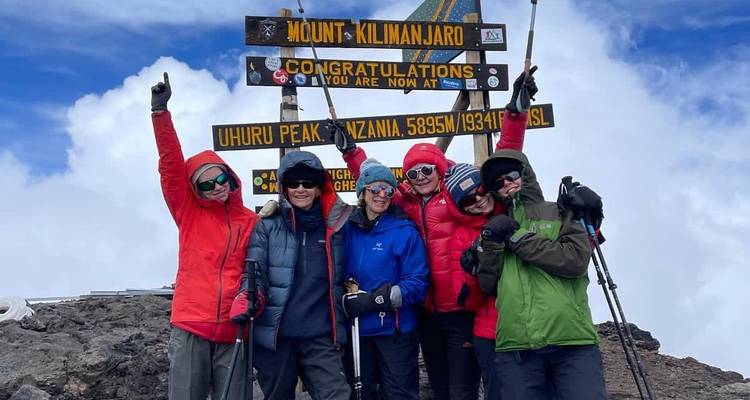 Group celebrating with trekking poles under the Uhuru Peak sign.