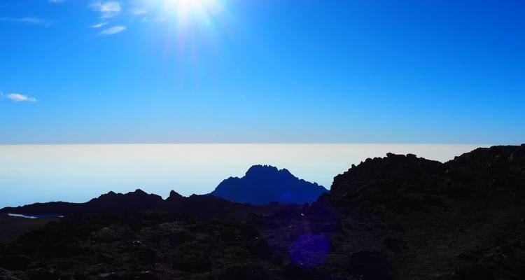 Silhouette of mountain peaks under a bright sun.