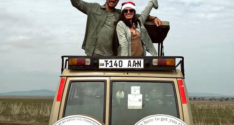 Dos personas posando encima de un vehículo de safari, una llevando un gorro festivo de Santa.
