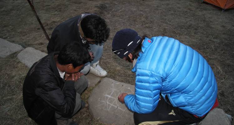 Drie mensen die op de grond zitten, tekenend op een platte steen.