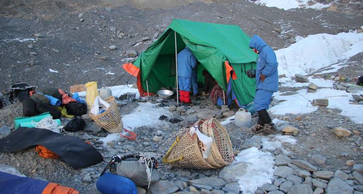 Kampeerders die tenten opzetten in een rotsachtig en besneeuw berggebied.