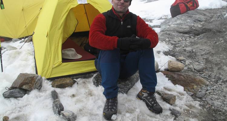 Person, die vor einem Zelt in einem schneebedeckten Bergcamp sitzt.
