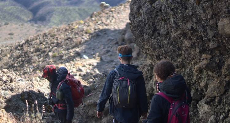 Een groep wandelaars die langs een rotsachtig bergpad loopt.