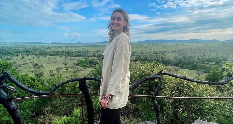 Una persona sonriendo en un balcón con vista a un vasto paisaje verde.