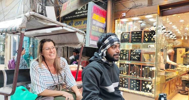 Una turista montando en un auto-rickshaw junto al conductor a través de un bazar de joyas lleno de brillantes exhibiciones de oro.