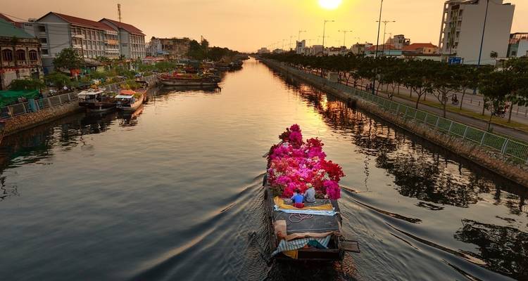 Barco en un canal con flores rosadas vibrantes durante el atardecer.