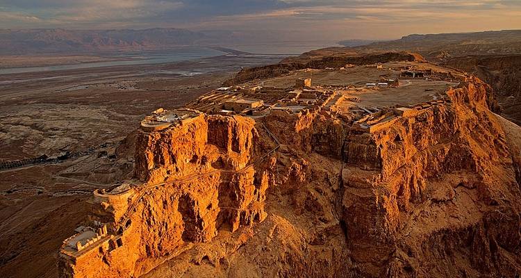 Aerial view of Masada fortress at sunrise, showing ancient ruins on a rocky plateau.