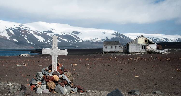 Edificio abandonado con un memorial de cruz en un paisaje árido y nevado.