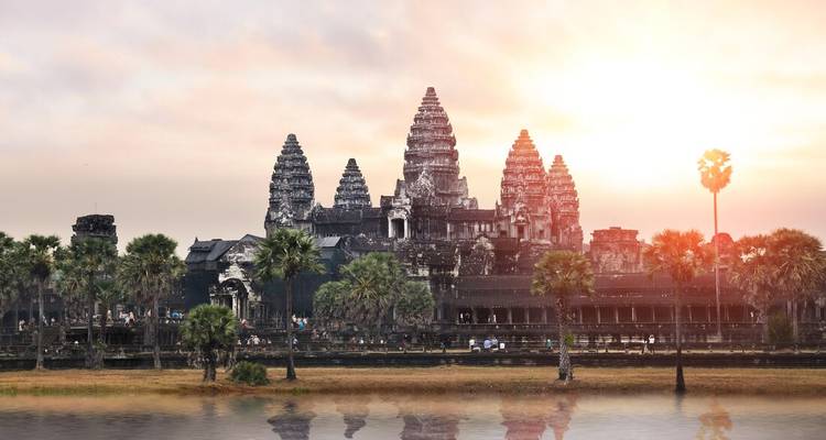 Iconic Angkor Wat temple complex back-lit by rising sun reflected in water.