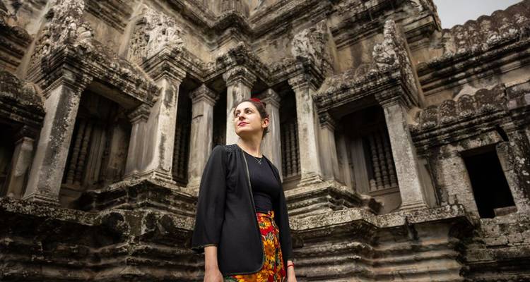 Female traveler gazes upward inside ornate stone gallery of Angkor Wat.