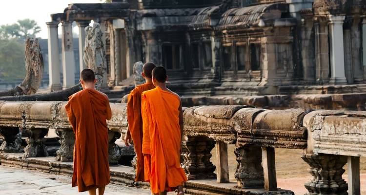 Buddhist monks in orange robes walk along ancient stone causeway at Angkor temple.