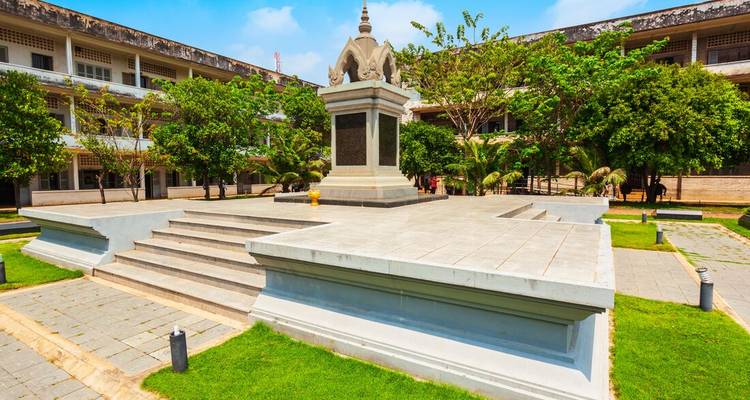 Memorial stupa and courtyard at Tuol Sleng Genocide Museum under blue sky.