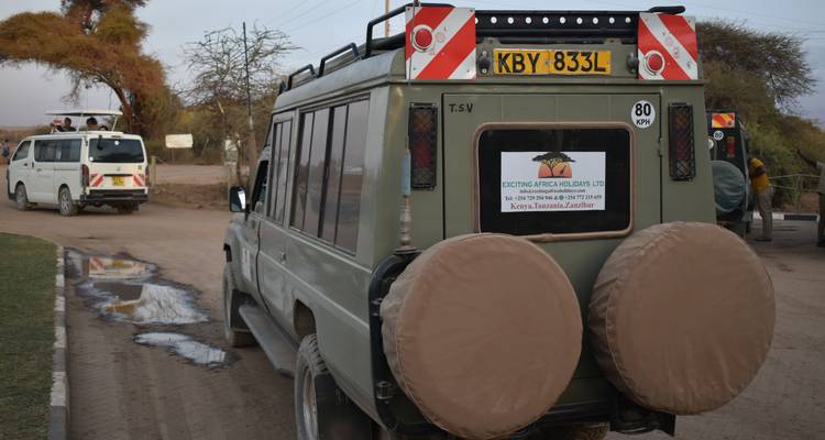 Safari-Fahrzeuge in einer Parklandschaft mit Beschilderung.