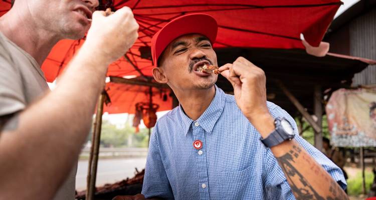 Un hombre disfrutando comida callejera bajo una sombrilla roja vibrante.