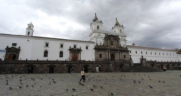 Large white church with people and pigeons in the square.