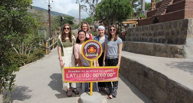 Grupo de personas paradas en la línea del Ecuador con un monumento.