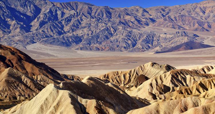 Weite Aussicht über die erodierten Badlands und den Wüstenboden vom Zabriskie Point unter einem tiefblauen Himmel im Death Valley.