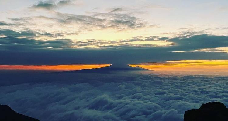 Ein Sonnenuntergang über Wolken mit einem entfernten Berg.