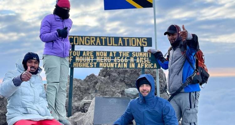 Eine Gruppe von Menschen auf dem Gipfel des Mount Meru mit einem Schild, das die Höhe anzeigt.