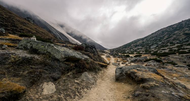 Vue panoramique d'un sentier de montagne sous un ciel nuageux.