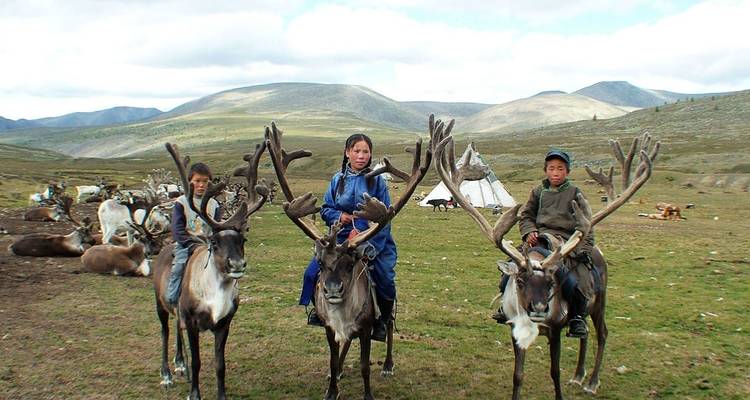 Kinder, die Rentiere in einer bergigen Landschaft reiten.