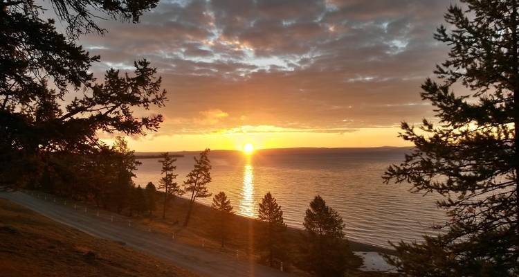 Sonnenuntergangsblick über einen See mit Bäumen im Gegenlicht.