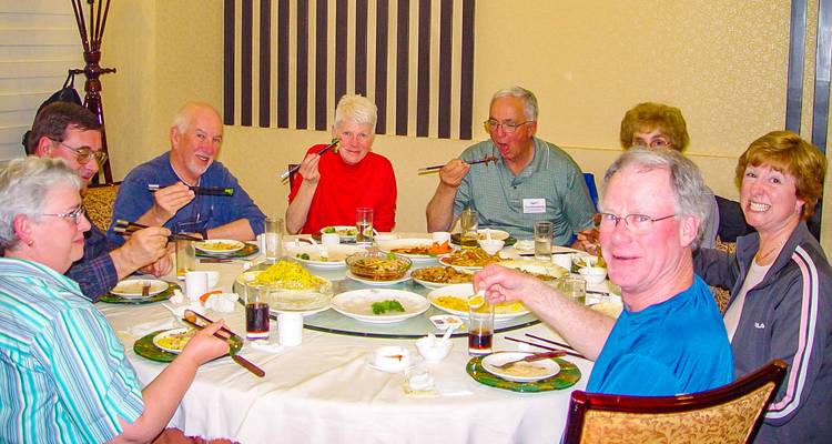 Group of people dining at a table with various dishes using chopsticks.