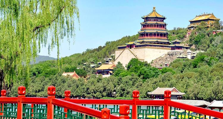 La colorida torre del Palacio de Verano se eleva sobre colinas boscosas y un puente rojo en Pekín bajo un cielo despejado.