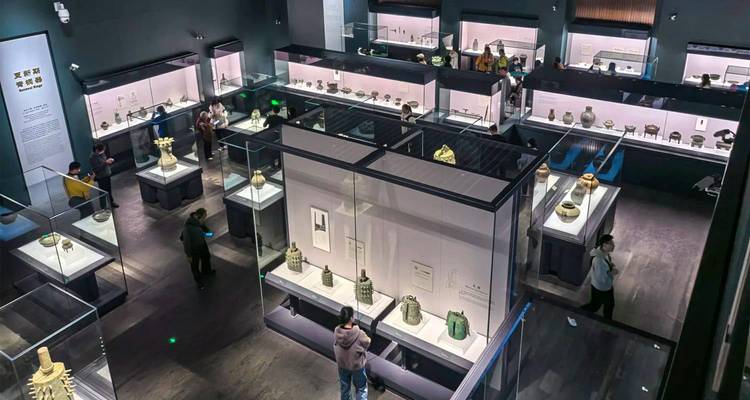 Los visitantes exploran vitrinas de cerámica antigua dentro de una galería de museo moderna y con poca luz.