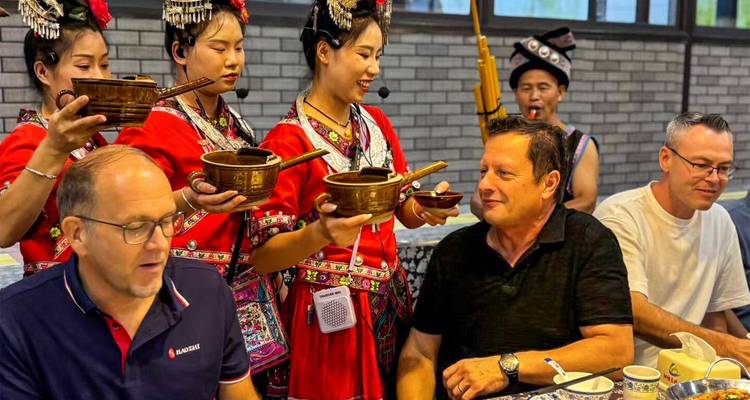 Les femmes de la minorité Miao, vêtues de robes traditionnelles rouge vif, servent des tasses en bois remplies d'alcool aux hôtes étrangers assis.