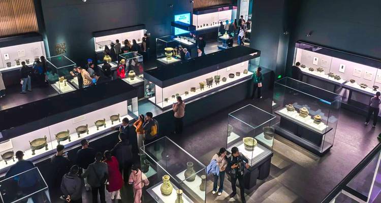 Vue aérienne de visiteurs de musée explorant des expositions de vases en bronze antiques dans des vitrines en verre.