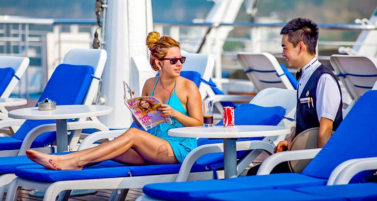 Femme se détendant sur un bateau de croisière avec un serveur debout à proximité.