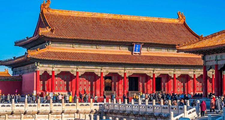 Los visitantes hacen fila a lo largo de balaustradas de mármol blanco frente a un salón de techo rojo y dorado en la Ciudad Prohibida de Beijing.