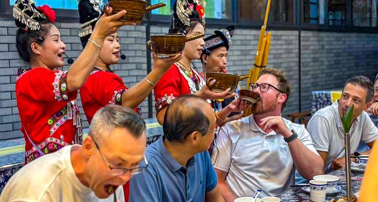 Los artistas Miao en traje rojo brindan con los comensales visitantes usando cuencos de madera durante un animado banquete.