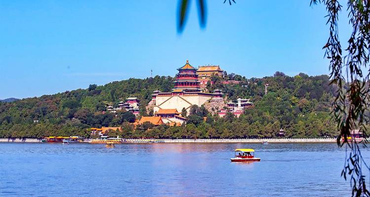 Vue panoramique du Palais d'Été de Pékin perché sur une colline luxuriante surplombant un lac bleu avec de petits bateaux de tourisme sur l'eau sous un ciel dégagé