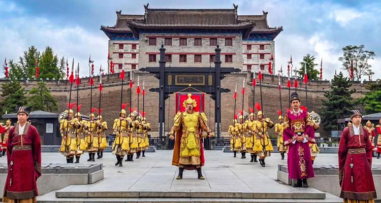 Reconstitution historique en costumes avec des soldats en armure dorée défilant devant la porte imposante de la muraille de la ville de Xi'an