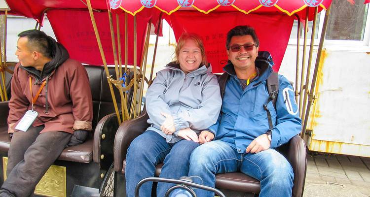 Zwei Touristen sitzen in einer Rikscha mit einem Fahrer.