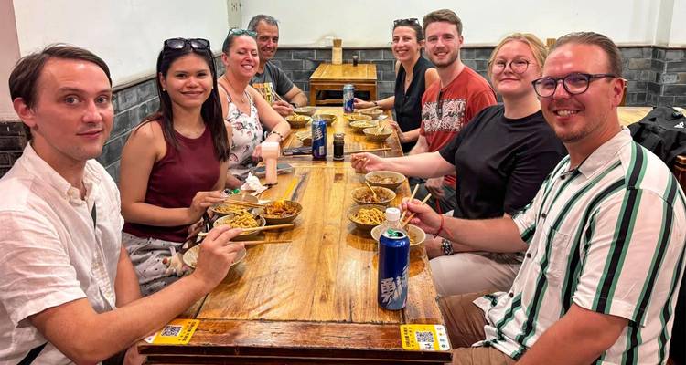Travel group enjoys bowls of noodles and beer around a wooden table inside a local Chinese eatery.