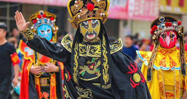 Vibrant Sichuan opera performers in ornate masks and flowing black and gold costumes parade through a street.