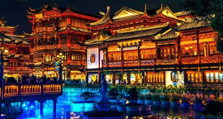 Historic pavilions of Shanghai’s Yu Garden illuminated and mirrored in tranquil pond water at night.