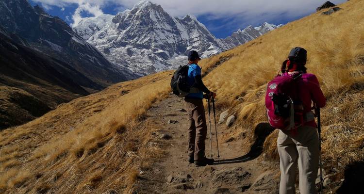 Hikers on a trail with snow-capped mountains.