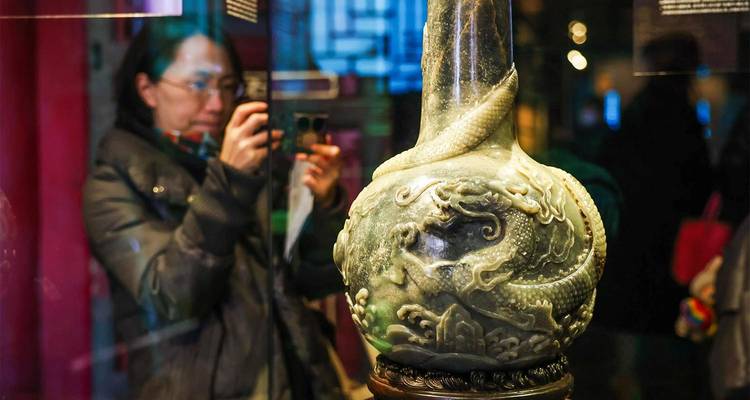 Un visiteur photographiant un vase en jade finement sculpté exposé derrière une vitre de musée.